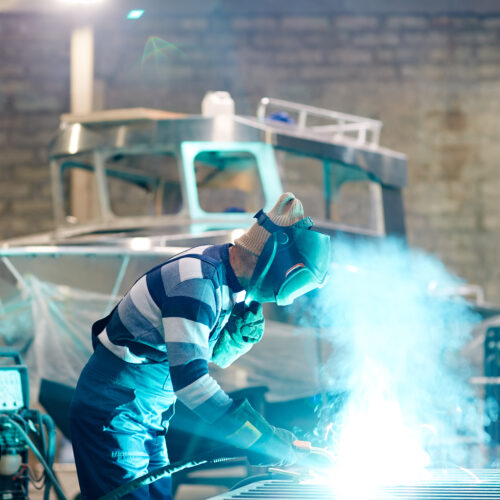 A man welding in a warehouse with fumes coming out.